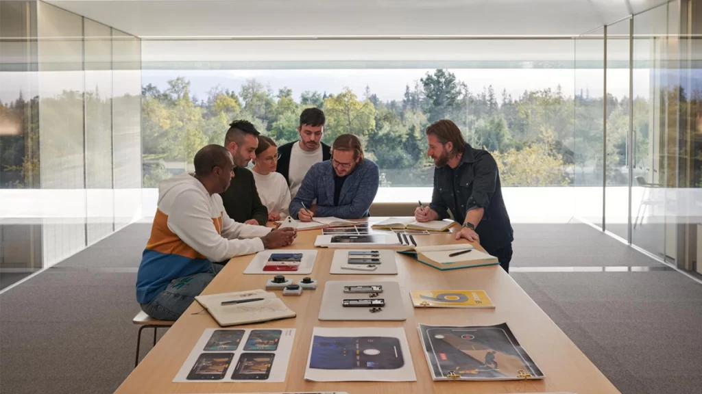 Apple designers working in an office with full width glass windows, looking through a variety of iPhone designs.