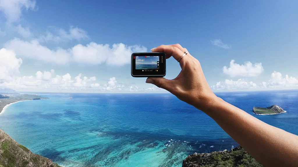 A GoPro action camera being held by a hand picturing a ombre blue ocean coastline on sunny day with distant clouds.