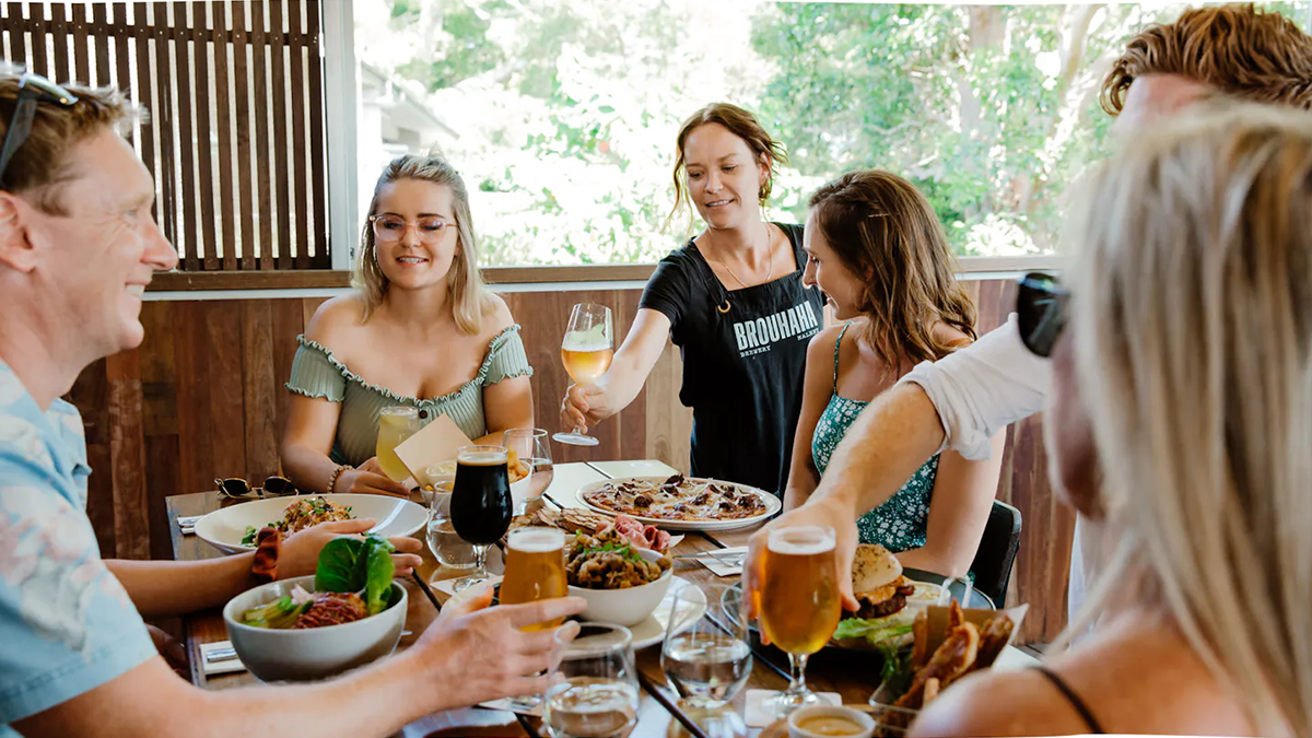 A group of friends are eating lunch at an outdoor venue. The waiter is passing over a glass of rosè.