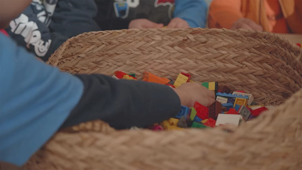 A toddler places in arm into a bamboo basket full of lego at Evoke Early Learning.