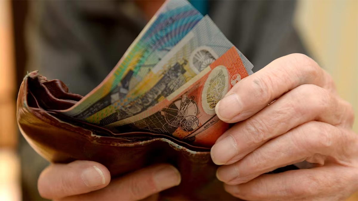 An elderly man holding a handful of Australian $10 and $20 notes.