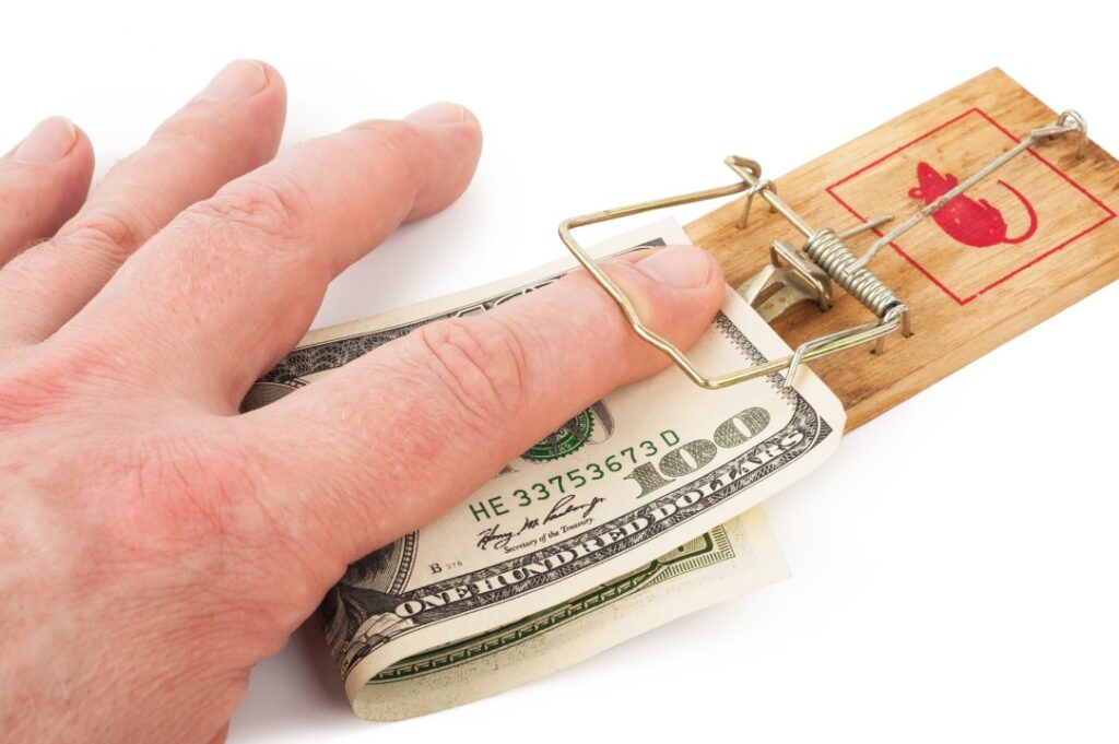 A human finger trapped under a mouse trap containing a one hundred dollar bill.