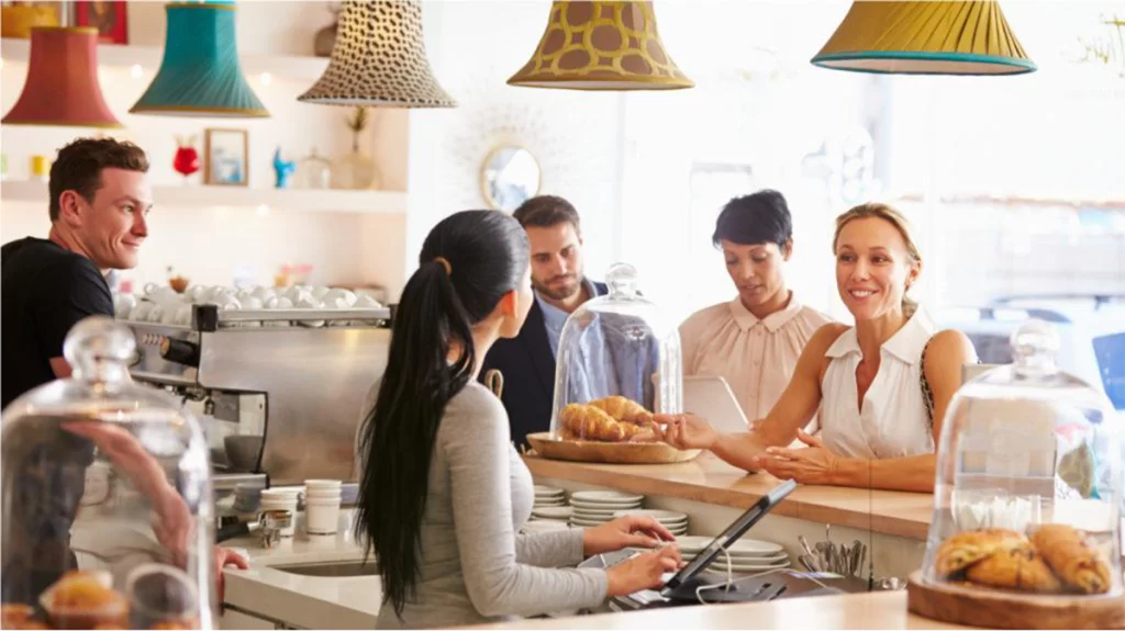 A young blonde woman ordering from the counter of a coffee shop. Croissants can be seen in the middle and right of frame.