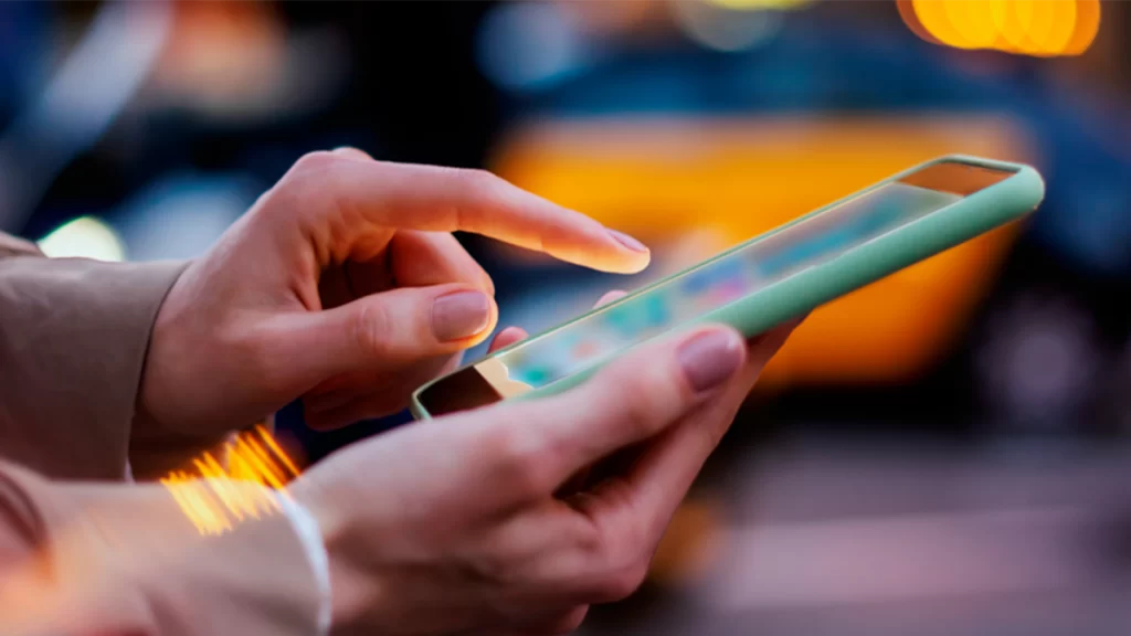 A male in a beige suit scrolling through their phone in a city street at night.