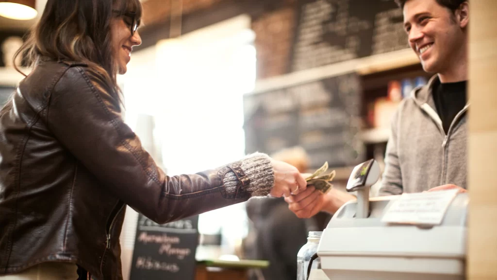 A middle aged woman handing over cash to a male cashier at a cafe.