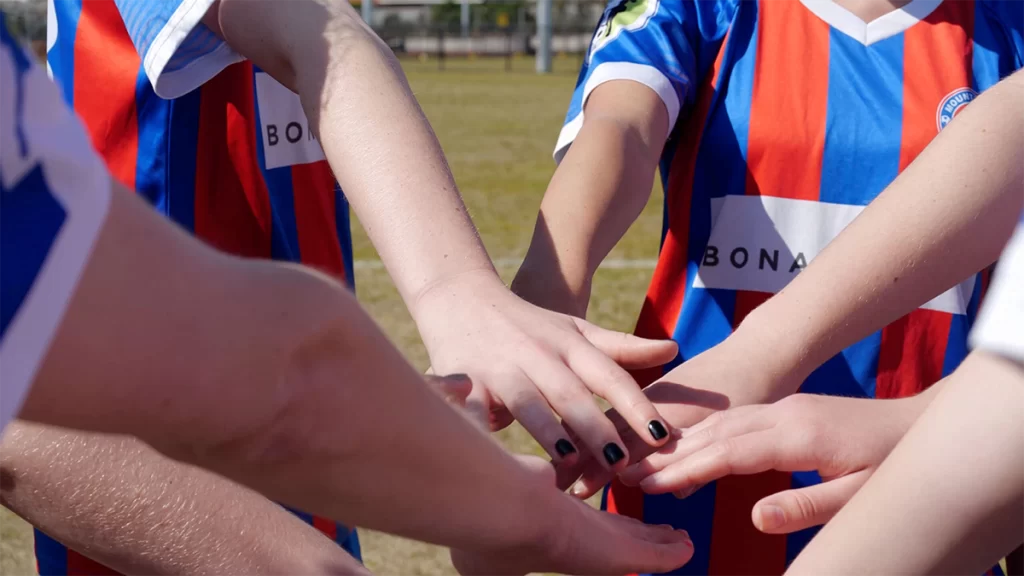 6 young girls from the Mount Martha Soccer Club create a circle and place their right hands in the middle on top of each other.